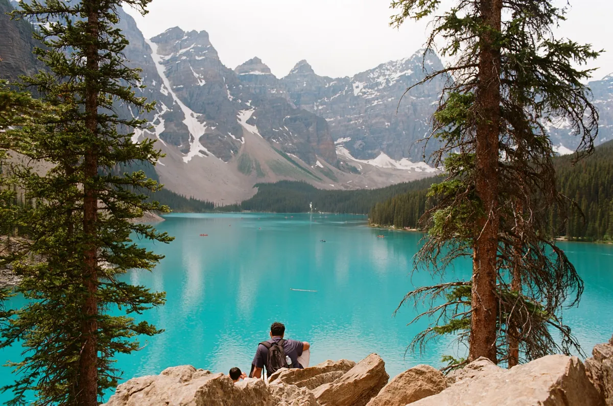 A man and his child sitting on a rock looking over Moraine Lake. Shot on Ektar 100