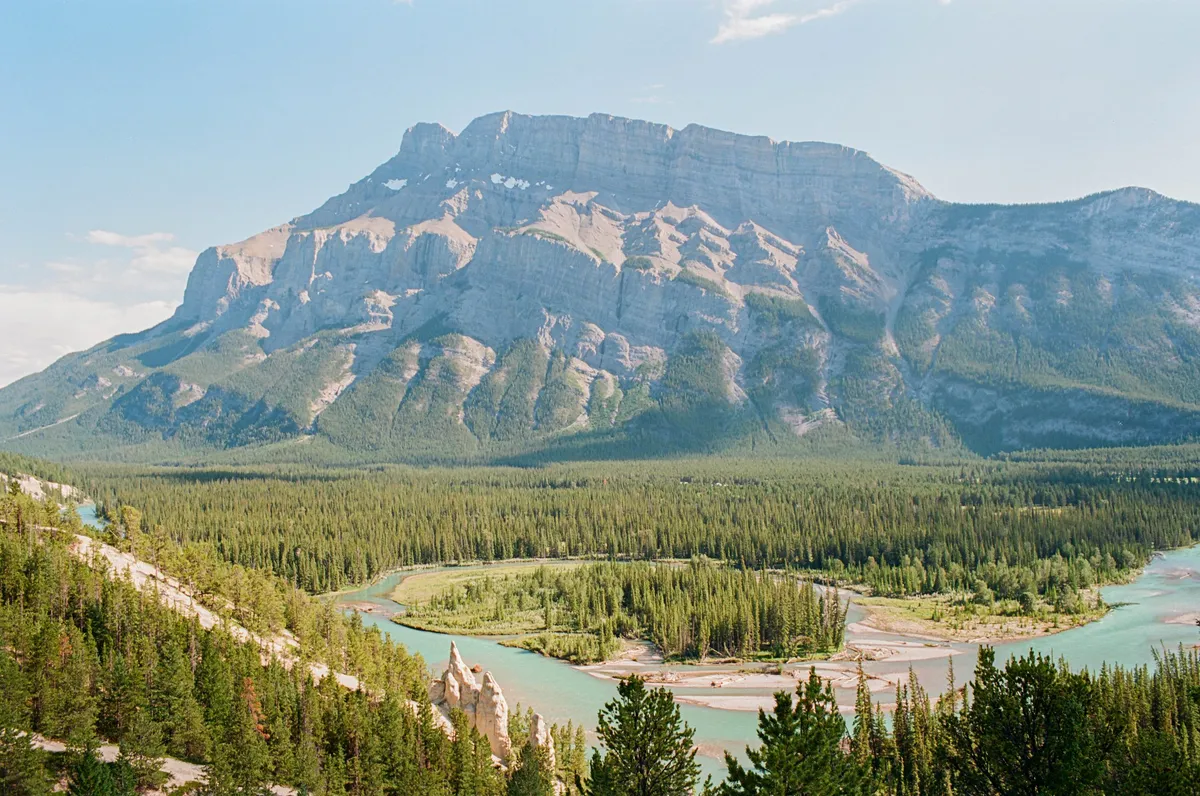 Shot from a viewpoint looking into a valley with hoodoos, a river, and Mount Rundle in the background. Banff, Alberta